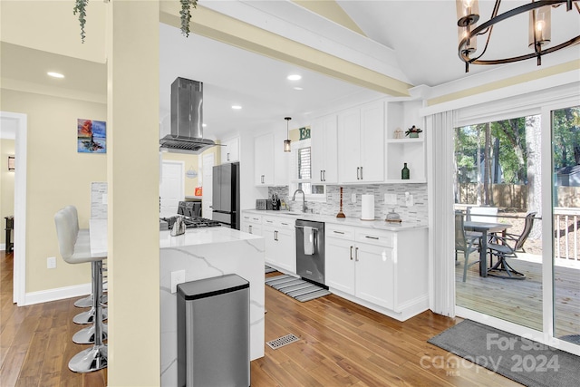 kitchen with white cabinetry, light stone countertops, island range hood, appliances with stainless steel finishes, and light wood-type flooring