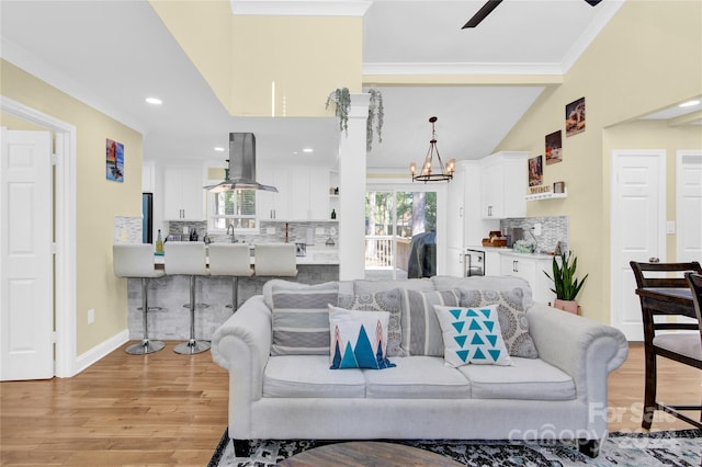 living room featuring crown molding, light hardwood / wood-style flooring, ceiling fan with notable chandelier, and vaulted ceiling