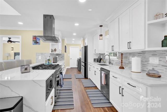 kitchen with light stone counters, hardwood / wood-style floors, decorative light fixtures, island range hood, and appliances with stainless steel finishes