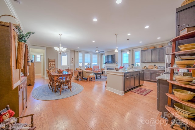 kitchen featuring a center island with sink, decorative light fixtures, light wood-type flooring, ornamental molding, and ceiling fan with notable chandelier