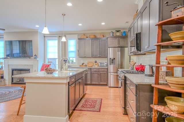 kitchen featuring appliances with stainless steel finishes, hanging light fixtures, a kitchen island with sink, light stone counters, and crown molding