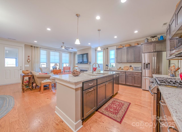 kitchen with appliances with stainless steel finishes, decorative light fixtures, backsplash, light stone counters, and a center island with sink