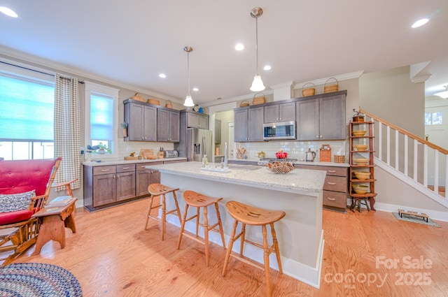 kitchen with stainless steel appliances, tasteful backsplash, a kitchen island with sink, decorative light fixtures, and a breakfast bar