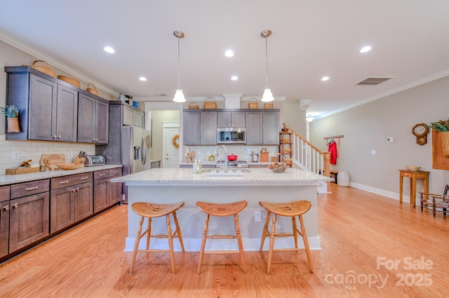 kitchen featuring stainless steel appliances, decorative backsplash, a center island with sink, and decorative light fixtures