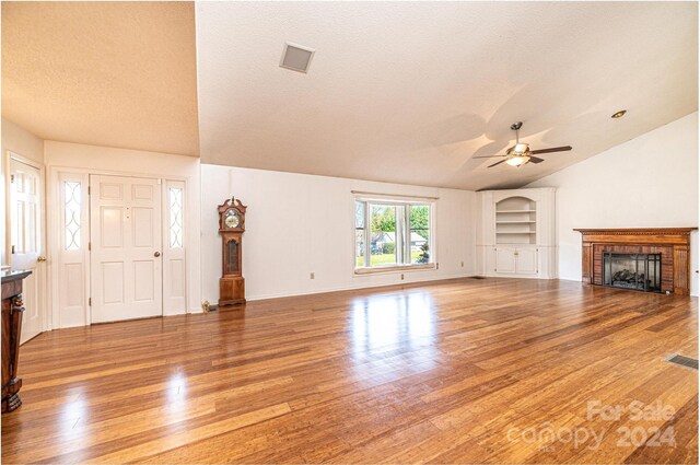 unfurnished living room with ceiling fan, a brick fireplace, vaulted ceiling, a textured ceiling, and hardwood / wood-style flooring