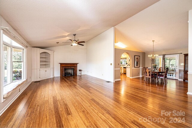 unfurnished living room featuring ceiling fan with notable chandelier, a healthy amount of sunlight, lofted ceiling, and hardwood / wood-style flooring