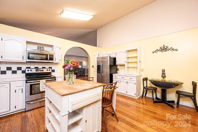 kitchen featuring lofted ceiling, backsplash, light wood-type flooring, appliances with stainless steel finishes, and white cabinetry