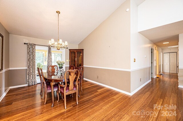 dining area with high vaulted ceiling, dark wood-type flooring, a textured ceiling, and an inviting chandelier