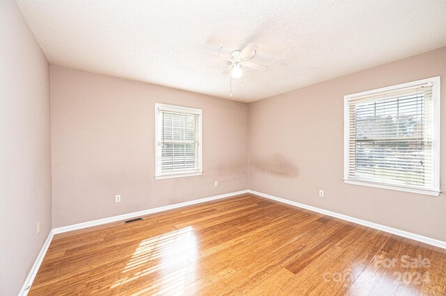 spare room with a textured ceiling, hardwood / wood-style flooring, a wealth of natural light, and ceiling fan