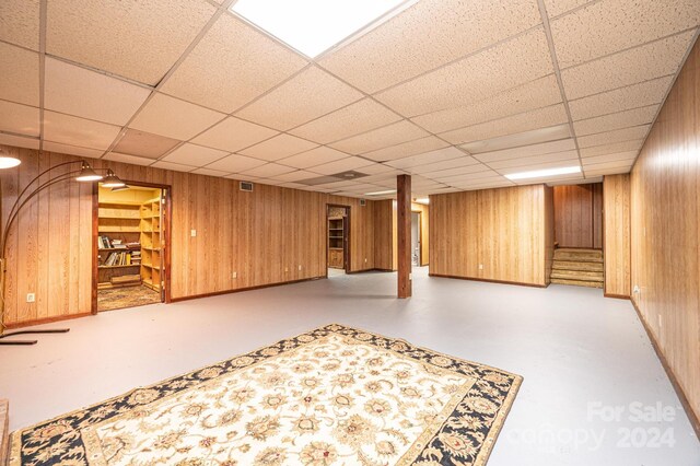 basement with a drop ceiling and wooden walls