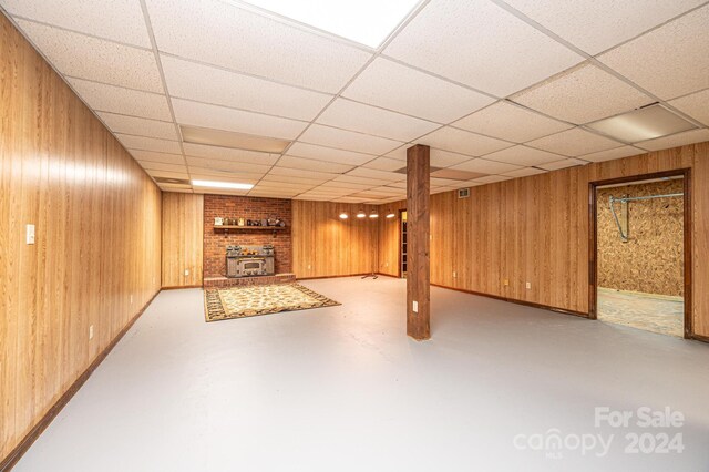 basement featuring a paneled ceiling, a wood stove, and wooden walls