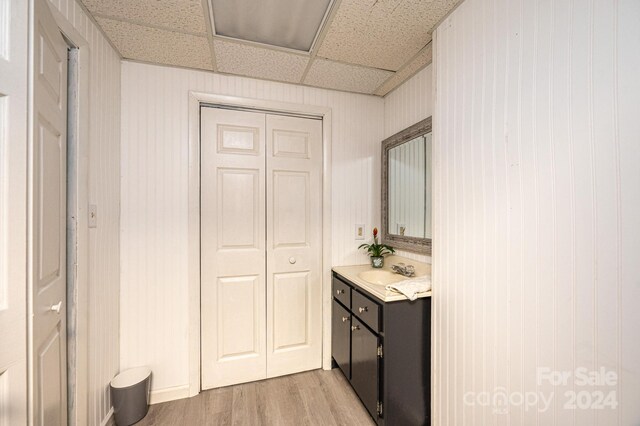 bathroom with a paneled ceiling, wood walls, vanity, and wood-type flooring