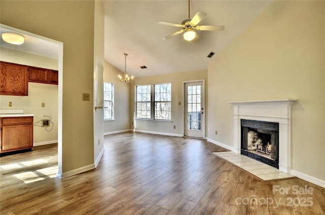 unfurnished living room with a tiled fireplace, high vaulted ceiling, ceiling fan with notable chandelier, and light wood-type flooring