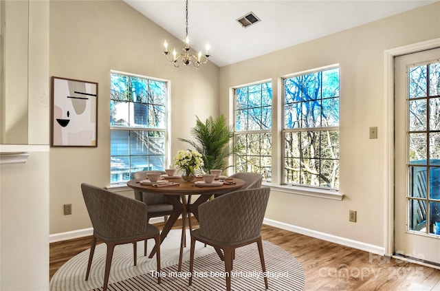 dining space with hardwood / wood-style flooring, lofted ceiling, and a notable chandelier