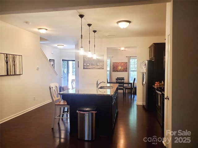 kitchen with a sink, range with electric stovetop, a breakfast bar area, light stone counters, and a kitchen island with sink