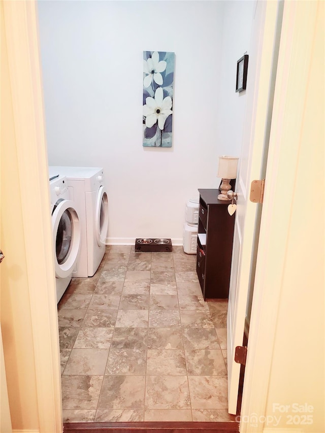 washroom featuring washing machine and clothes dryer, baseboards, and light stone finish floors