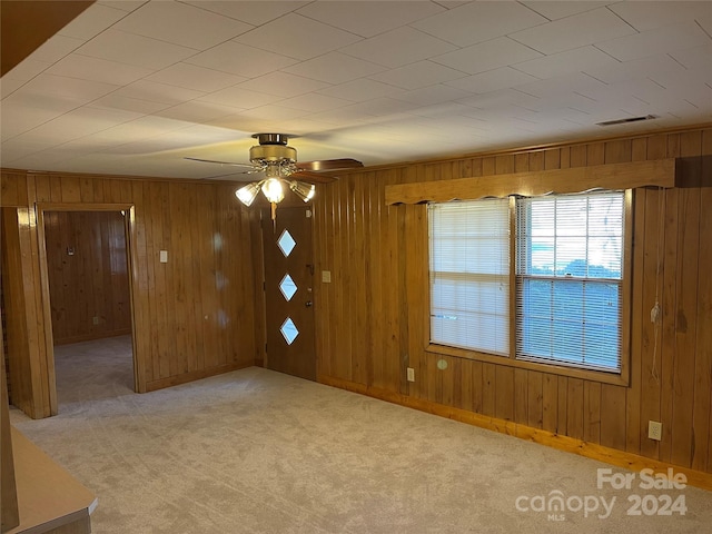 unfurnished room with ceiling fan, light carpet, and wooden walls