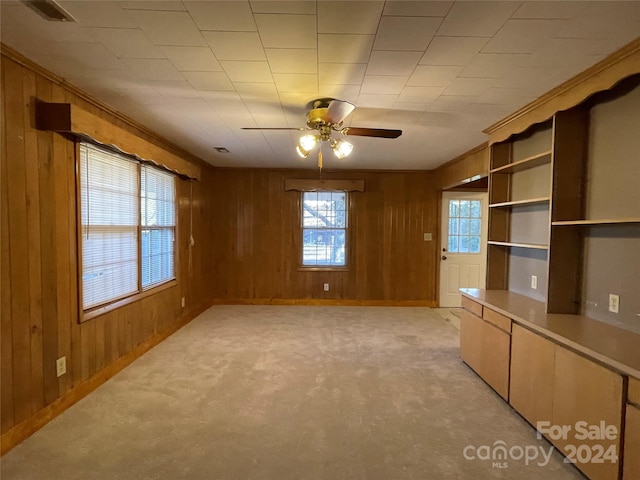 interior space featuring wooden walls, ceiling fan, light carpet, and ornamental molding