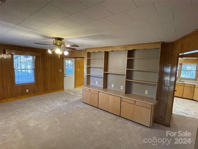 unfurnished living room featuring light colored carpet, ceiling fan, and wood walls