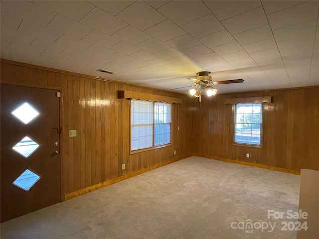 carpeted foyer with wood walls and ceiling fan