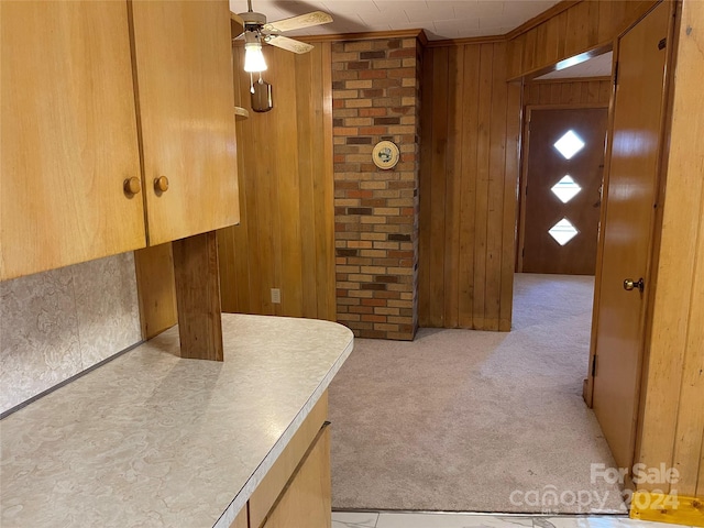 kitchen featuring light colored carpet, ceiling fan, and wood walls