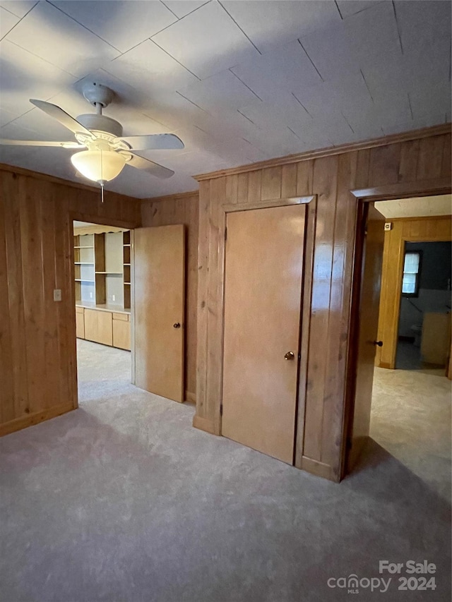 unfurnished bedroom featuring ceiling fan, light carpet, and wooden walls