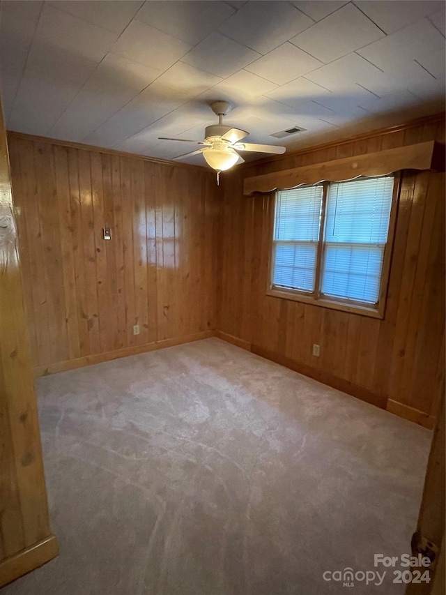 spare room with wooden walls, ceiling fan, and light colored carpet