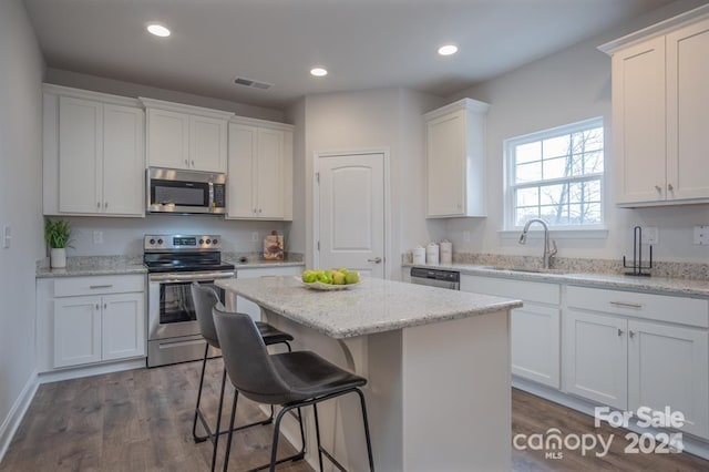 kitchen with a kitchen island, sink, white cabinets, light stone counters, and stainless steel appliances