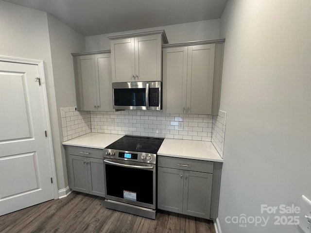 kitchen with tasteful backsplash, stainless steel appliances, dark wood-type flooring, and gray cabinetry