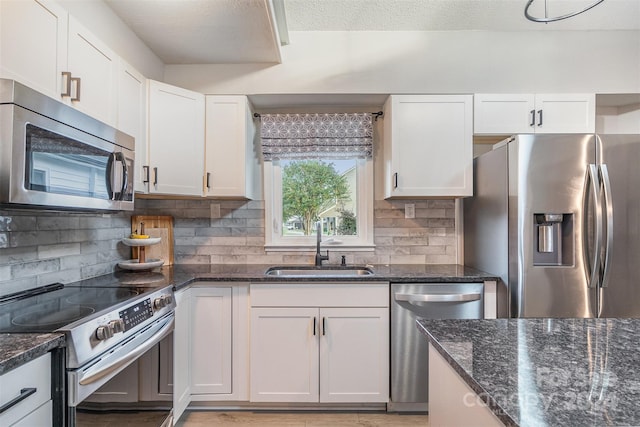 kitchen featuring white cabinetry, sink, stainless steel appliances, dark stone counters, and decorative backsplash