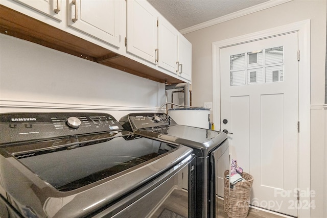 clothes washing area featuring crown molding, cabinets, a textured ceiling, and washing machine and dryer