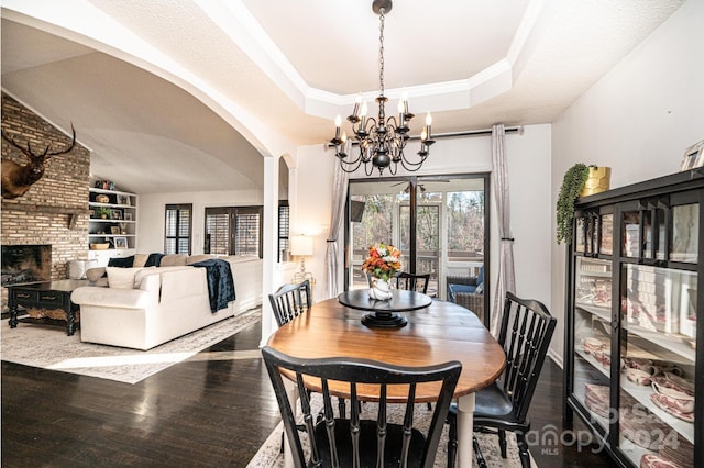 dining area featuring a tray ceiling, vaulted ceiling, an inviting chandelier, a fireplace, and hardwood / wood-style floors