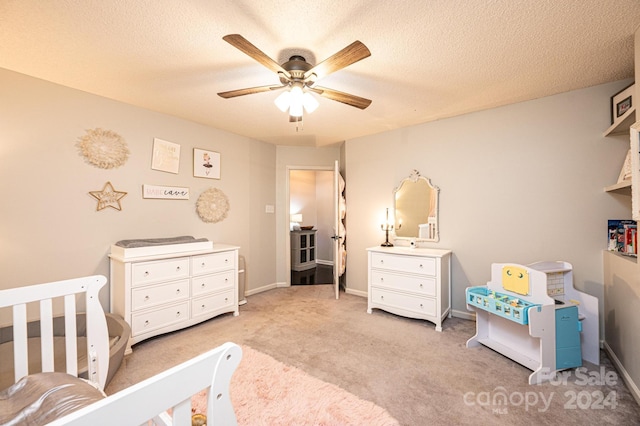 bedroom with light carpet, a textured ceiling, a nursery area, and ceiling fan