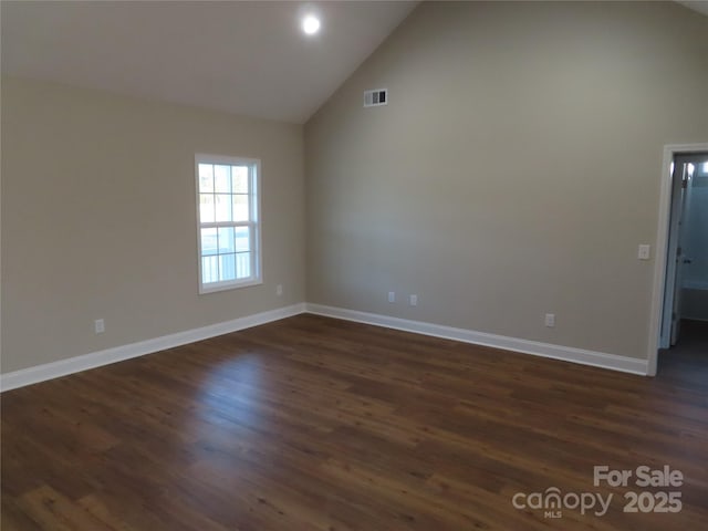 spare room with dark wood-type flooring and high vaulted ceiling