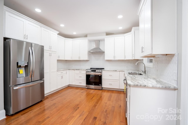 kitchen with sink, light hardwood / wood-style flooring, wall chimney exhaust hood, appliances with stainless steel finishes, and white cabinetry