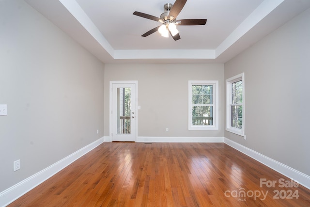 unfurnished room featuring hardwood / wood-style flooring, a raised ceiling, and a healthy amount of sunlight