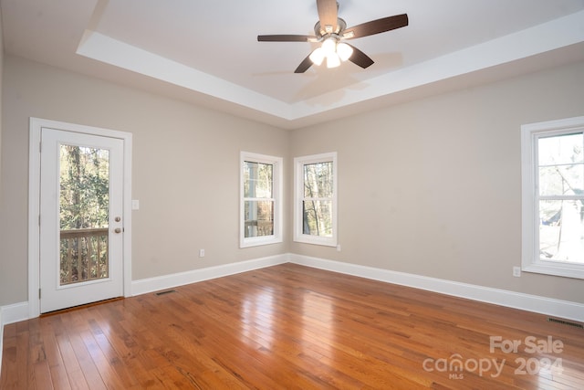 empty room with a tray ceiling, a wealth of natural light, and hardwood / wood-style floors