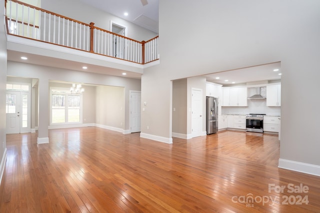 unfurnished living room featuring a chandelier, a towering ceiling, and light hardwood / wood-style flooring