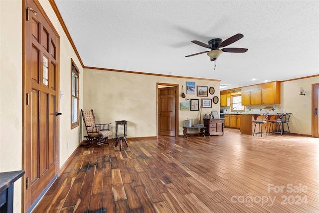 living room with a textured ceiling, crown molding, ceiling fan, and dark wood-type flooring