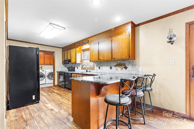 kitchen featuring black appliances, washing machine and dryer, light wood-type flooring, and kitchen peninsula