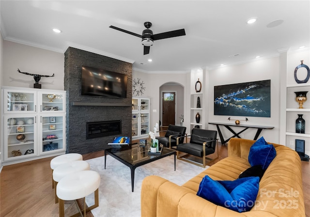 living room with a brick fireplace, light hardwood / wood-style flooring, built in features, and ornamental molding