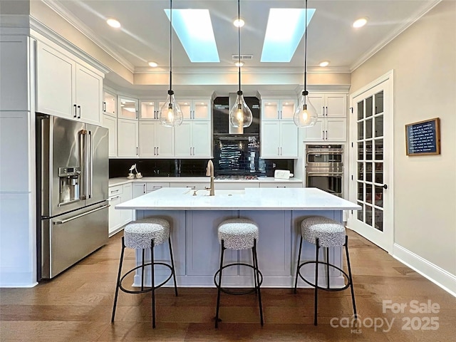 kitchen with a breakfast bar, pendant lighting, decorative backsplash, a kitchen island with sink, and stainless steel appliances