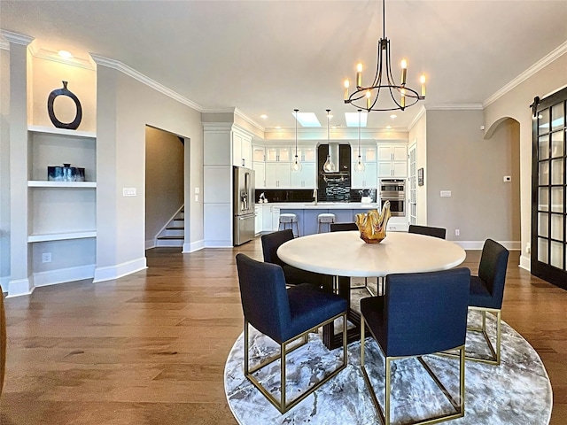 dining space with built in shelves, sink, crown molding, a chandelier, and hardwood / wood-style flooring