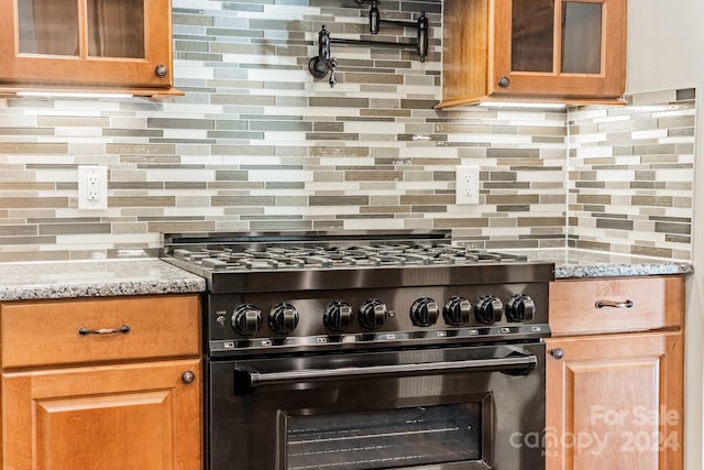 kitchen featuring light stone counters, high end stove, and backsplash