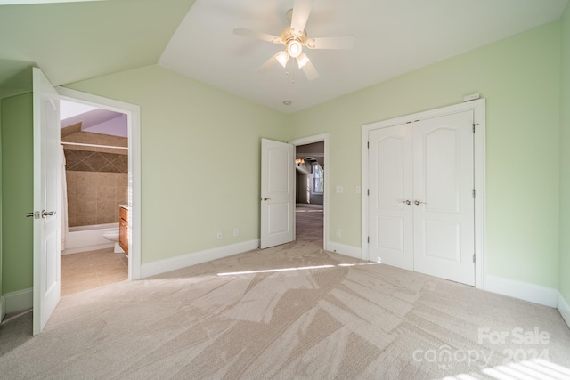 unfurnished bedroom featuring light carpet, ensuite bath, ceiling fan, a closet, and lofted ceiling