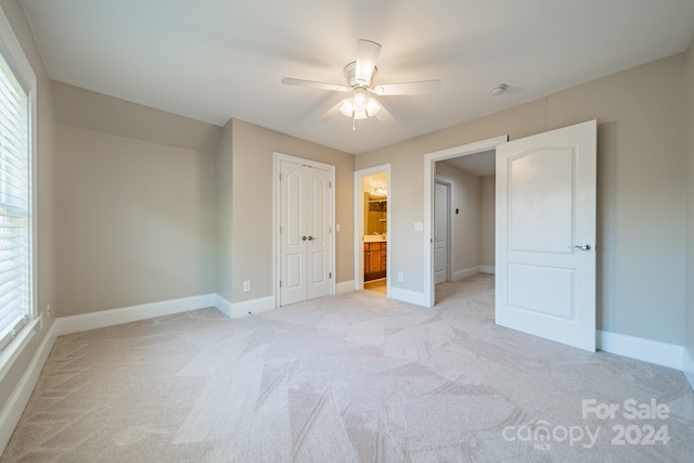 unfurnished bedroom featuring ensuite bath, ceiling fan, a closet, and light carpet