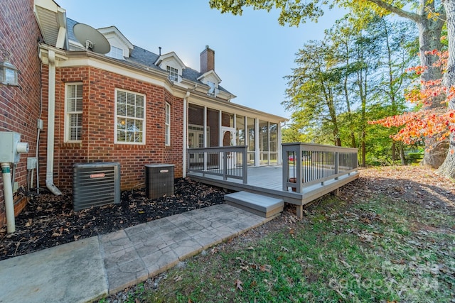 rear view of property featuring central air condition unit, a wooden deck, and a sunroom