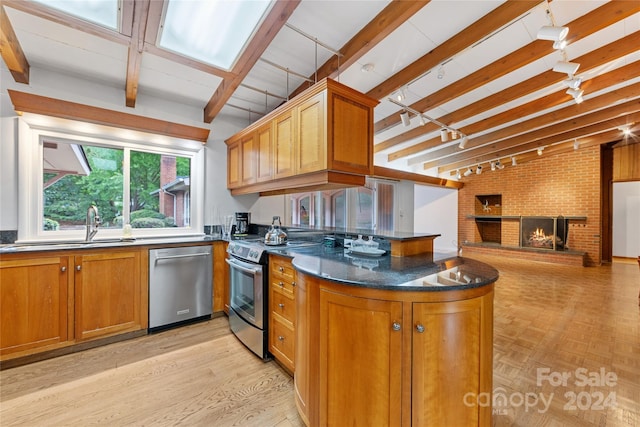 kitchen featuring brick wall, stainless steel appliances, light hardwood / wood-style flooring, dark stone countertops, and a fireplace