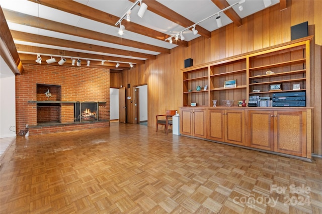 unfurnished living room featuring beam ceiling, wooden walls, a fireplace, and rail lighting