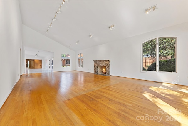 unfurnished living room featuring rail lighting, a fireplace, high vaulted ceiling, and light wood-type flooring